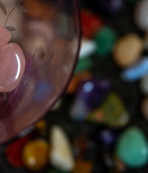 Close-up of rose quartz stones in glass with a blurred background of various colorful pebbles.